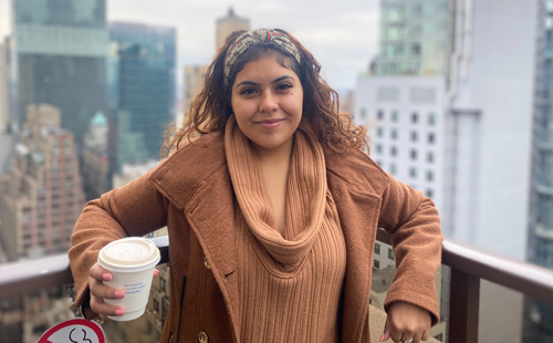 Nayelli Reyes on a balcony with a coffee and a city view in background